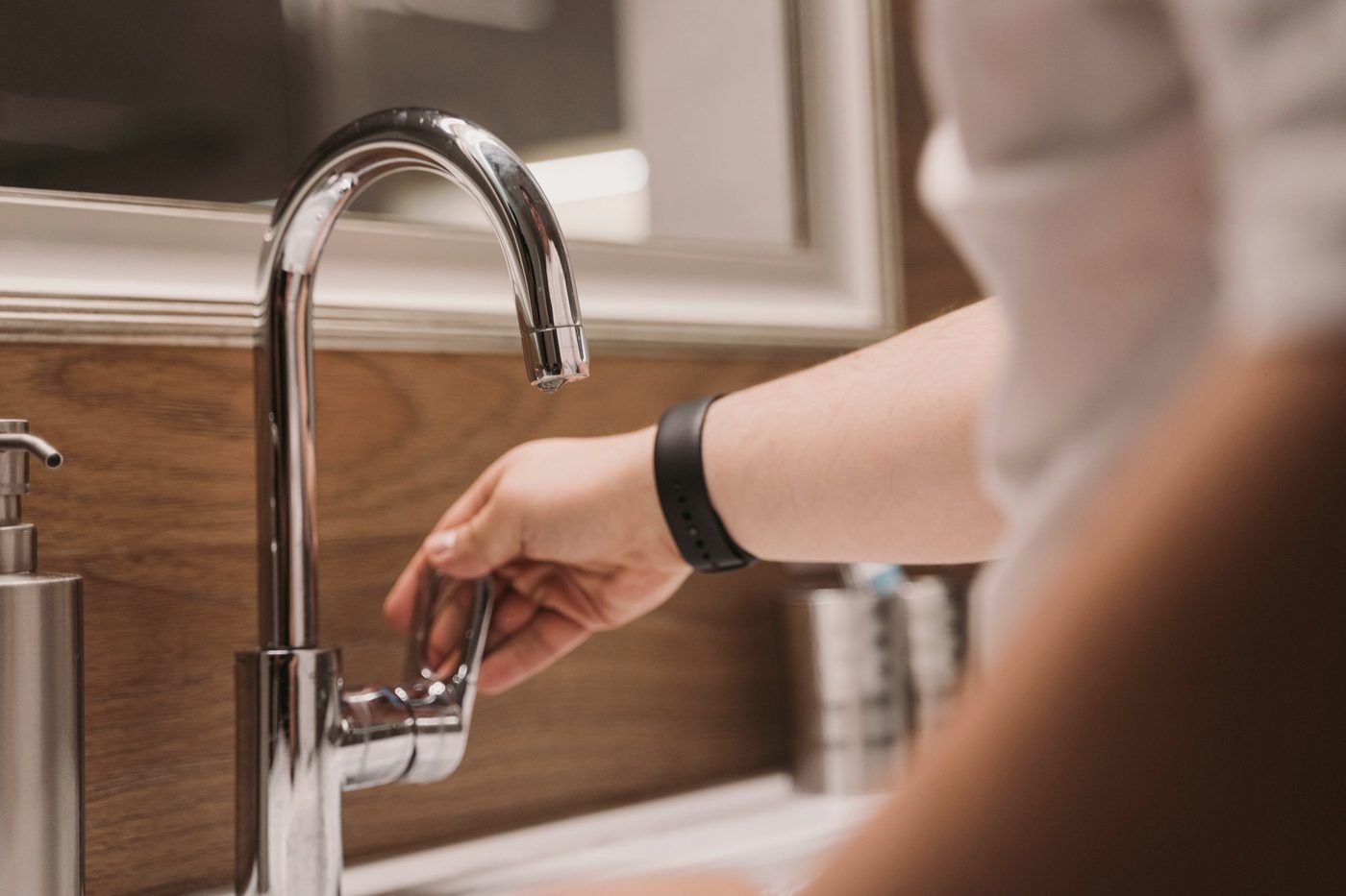 Hand adjusting a chrome faucet at a bathroom sink